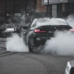Black BMW sports car driving during daytime emphasizing pollution issues.
