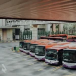 Group of electric buses with orange and white paint in a bus lot.