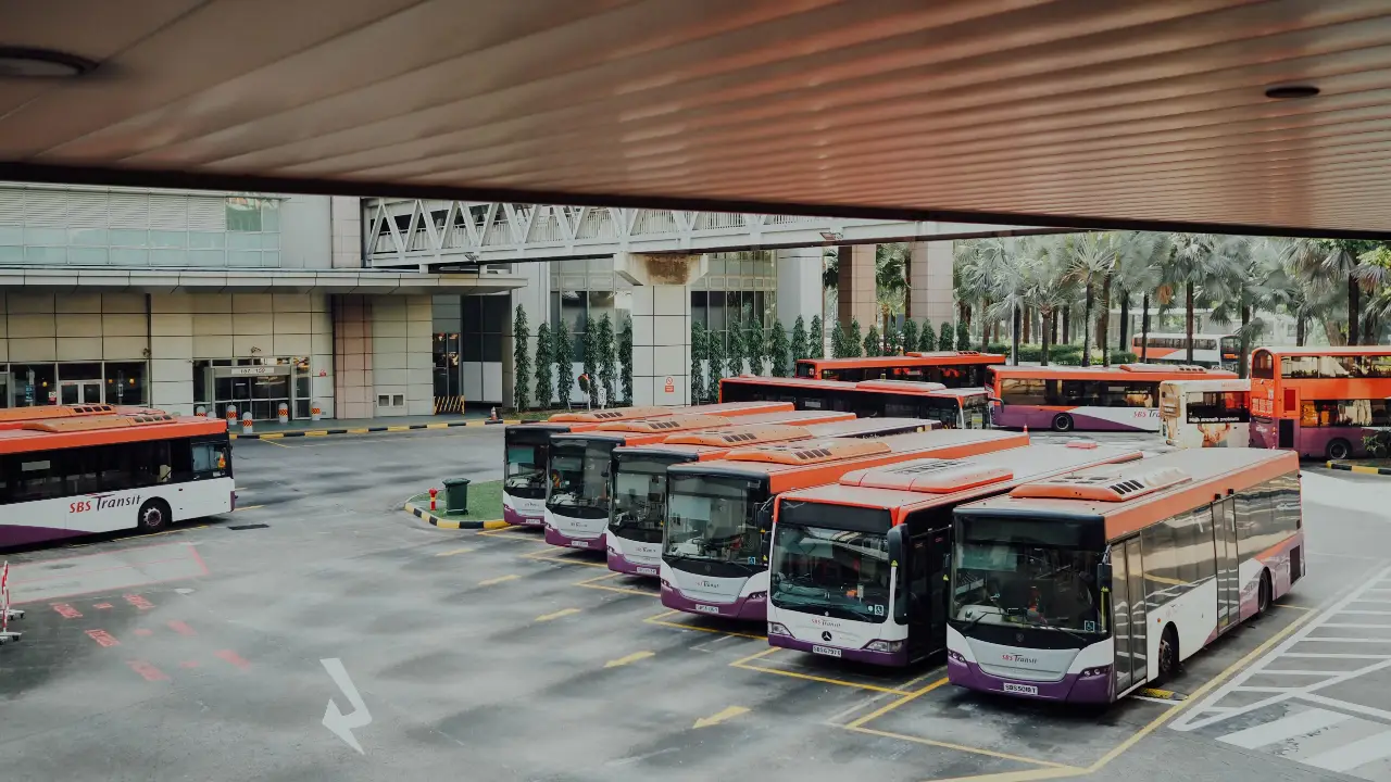 Group of electric buses with orange and white paint in a bus lot.