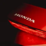 Honda logo glowing at night with a red motorbike nearby.