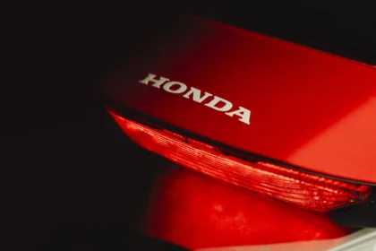 Honda logo glowing at night with a red motorbike nearby.