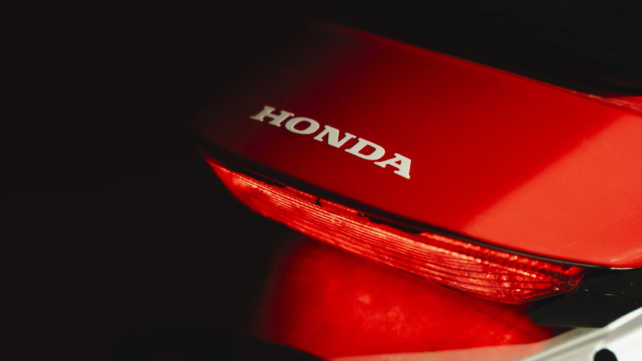 Honda logo glowing at night with a red motorbike nearby.