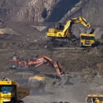 Excavators working at a mining site with rugged terrain in the background.