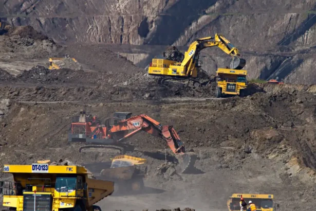 Excavators working at a mining site with rugged terrain in the background.