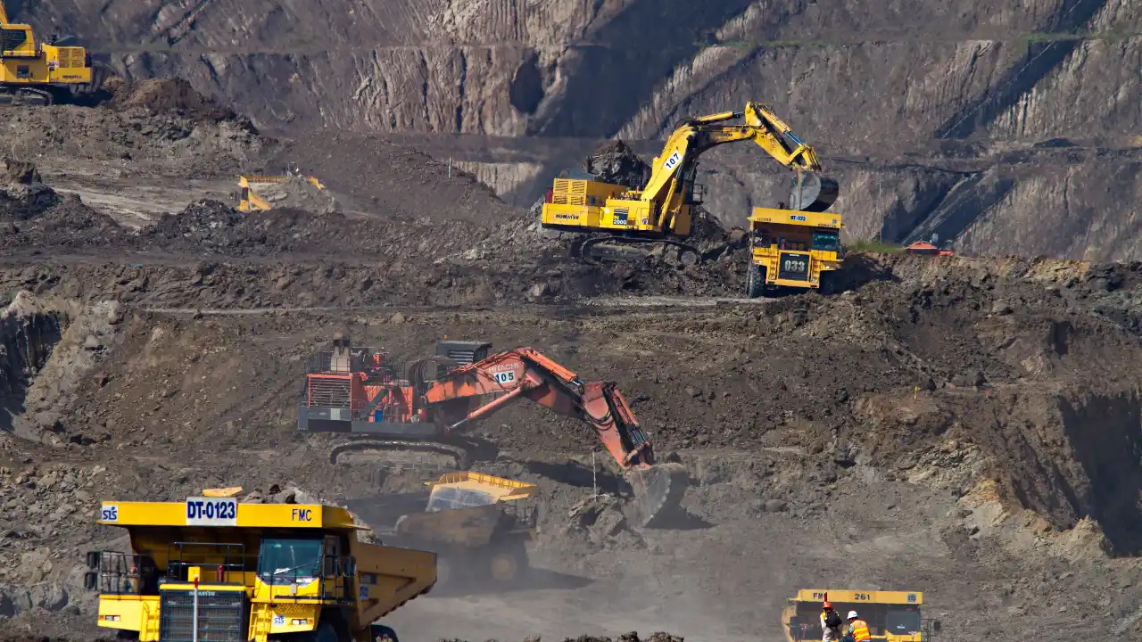 Excavators working at a mining site with rugged terrain in the background.