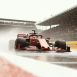 Red F1 car racing on wet track with water spray and spectators in rain