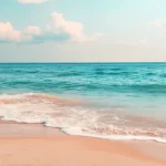 Quiet beach with golden sand, turquoise waters, and a bright sky.