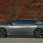 Silver electric car parked near trees on a roadside.