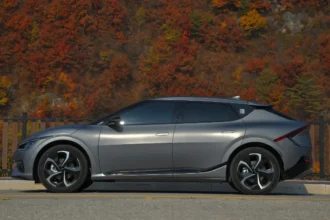 Silver electric car parked near trees on a roadside.