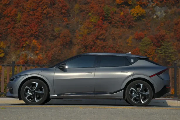 Silver electric car parked near trees on a roadside.