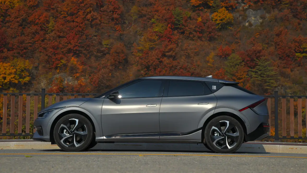 Silver electric car parked near trees on a roadside.