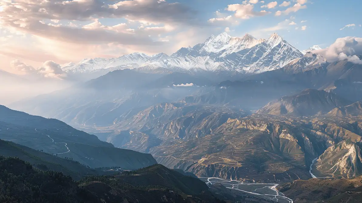 Snow-capped mountains with pastel sky over rolling hills and winding roads.