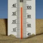 Thermometer in sand with a clear blue sky backdrop