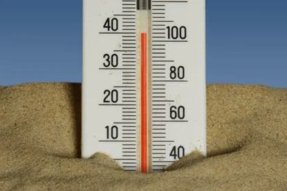 Thermometer in sand with a clear blue sky backdrop