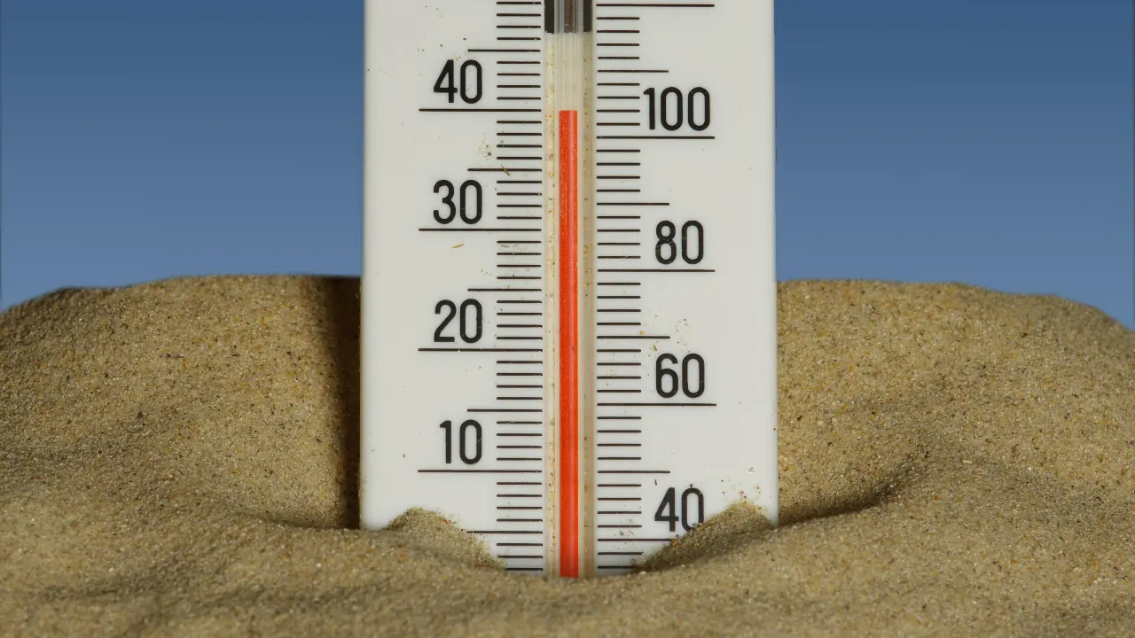 Thermometer in sand with a clear blue sky backdrop