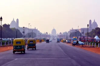 Street scene in New Delhi with tuk-tuks, cars, and people bustling.