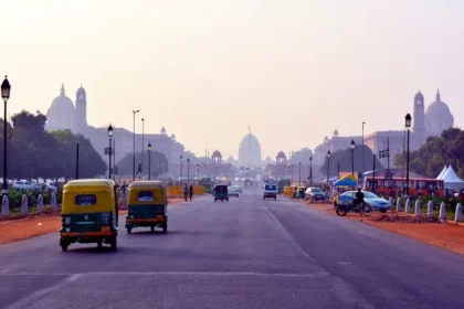 Street scene in New Delhi with tuk-tuks, cars, and people bustling.
