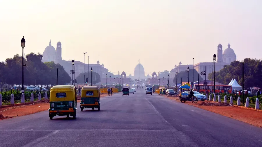 Street scene in New Delhi with tuk-tuks, cars, and people bustling.