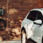 White car parked in front of wooden wall in outdoor setting.