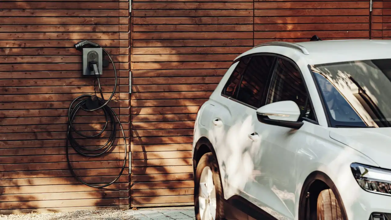 White car parked in front of wooden wall in outdoor setting.
