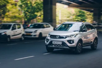 White Tata car driving on street next to a bridge in city environment