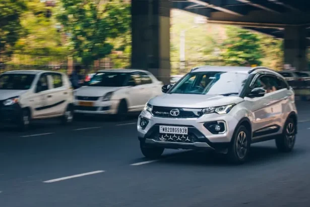 White Tata car driving on street next to a bridge in city environment