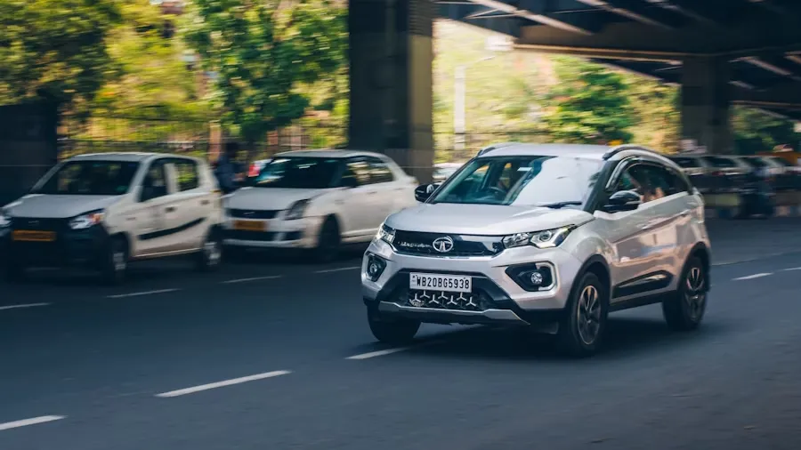 White Tata car driving on street next to a bridge in city environment
