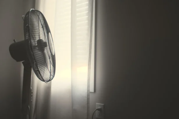 White wall fan running near white window blinds in hot bedroom.