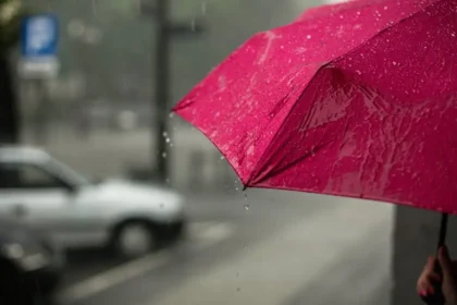 Women holding pink umbrellas during heavy rain in Delhi, India.