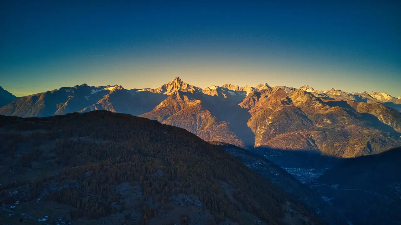 Swiss mountain range at sunset, rugged peaks with colorful sky.